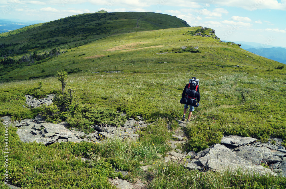 Young hiker climbing a rocky mountain trail, enjoying the warm sunshine