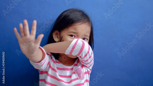 portrait of little sad fearful injured asian girl wearing pink stripped t-shirt sitting and covering mouth with arm.
