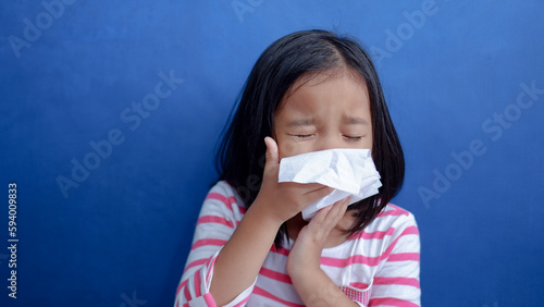 A cold girl blows her nose in a white rag on blue background. Influenza or Rhinitis snot runny nose stuffy nose. Allergy young asian girl holdingwhite  handkerchief. Medical concept.