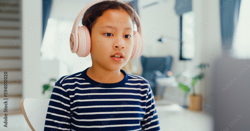 Asian toddler girl with sweater wear headphone sit front of desk with notepad use magic pen focus on writing do homework, finger counting number math online learning course from laptop at home. Asian toddler girl with sweater wear headphone sit front of desk with notepad use magic pen focus on writing do homework, finger counting number math online learning course from laptop at home.