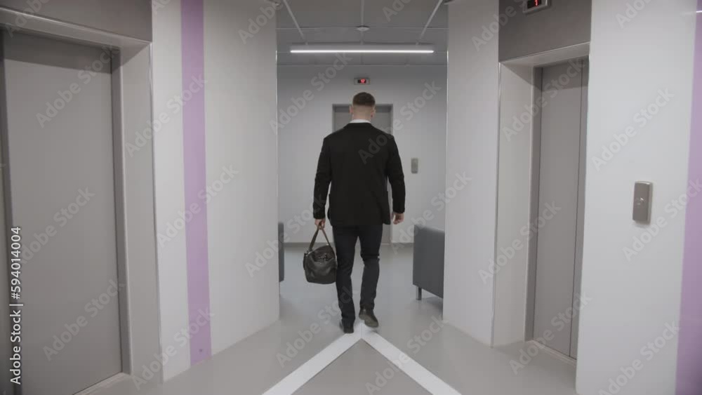 A man walks with a bag in his hand to the elevator A man walks with a bag in his hand to the elevator