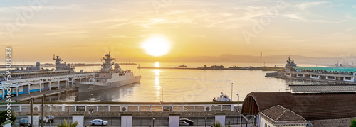 Fotografie Algerian Naval Forces coast guards vessels moored in the Port of Algiers city with trawlers sailing, cloudy bright sky at sunrise and the great mosque minaret