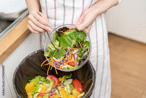 Compost from leftover food asian young housekeeper woman, female hand holding salad bowl use fork scraping waste, rotten vegetable throwing away into garbage, trash or bin. Environmentally responsible