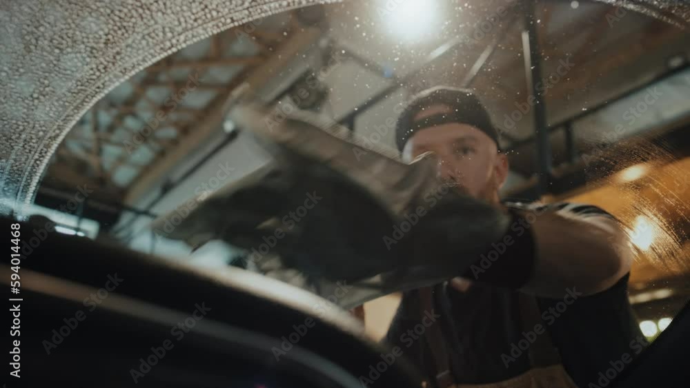 Low angle shot of auto mechanic washing front window with spay and cloth, view from car interior. Garage ceiling in background Low angle shot of auto mechanic washing front window with spay and cloth, view from car interior. Garage ceiling in background