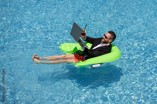 Summer business dreams. Business man in suit floating with cocktail and laptop in swimming pool. Summer business vacation. Funny crazy businessman rest in formal wear in pool. Hot summer business. © Volodymyr