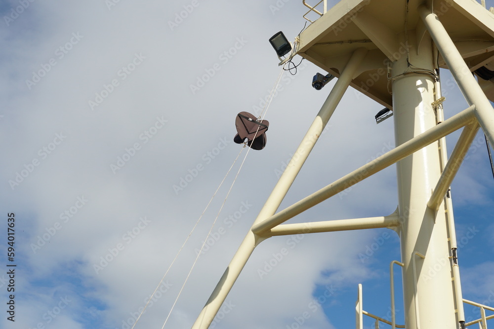Forward mast of vessel with one black anchor ball as day signal. There are also ladder and platform with surveillance camera and led light projectors. Behind is blue sky with clouds and copy space. Forward mast of vessel with one black anchor ball as day signal. There are also ladder and platform with surveillance camera and led light projectors. Behind is blue sky with clouds and copy space.