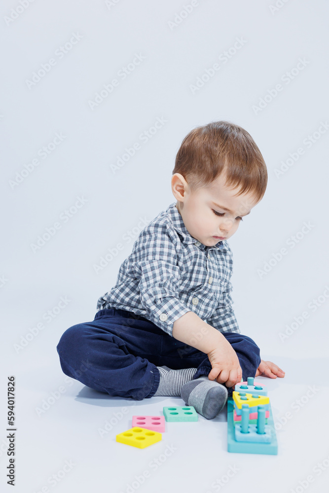 A cute little boy in a checkered shirt sits on a white background and plays with wooden educational toys. Ecological wooden toys for children A cute little boy in a checkered shirt sits on a white background and plays with wooden educational toys. Ecological wooden toys for children