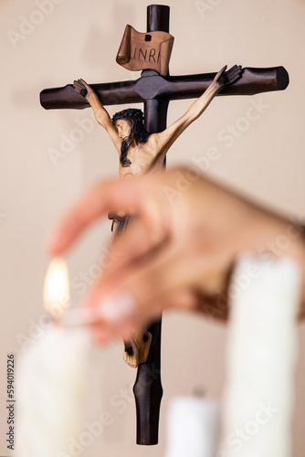 Hand lighting candles with a wooden crucifix in the background on brown background