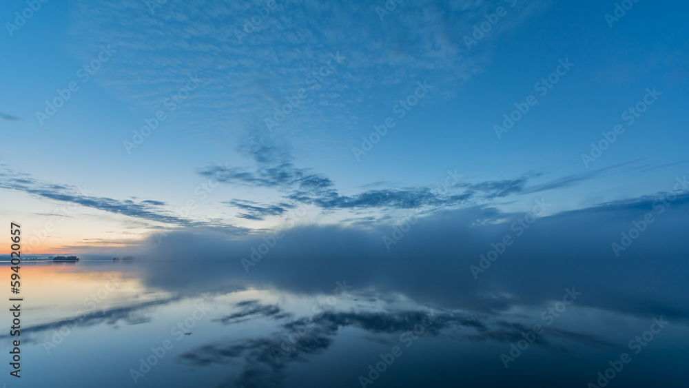 Summer lake scenery with clouds and mist reflected on the water in Finland