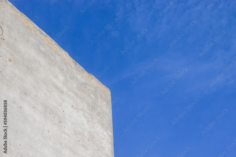 Bottom view of the corner of the building against the blue sky. Abstract view of the corner of the wall and the sky. Gray stucco wall against a bright sky. Bottom view of the corner of the building against the blue sky. Abstract view of the corner of the wall and the sky. Gray stucco wall against a bright sky.