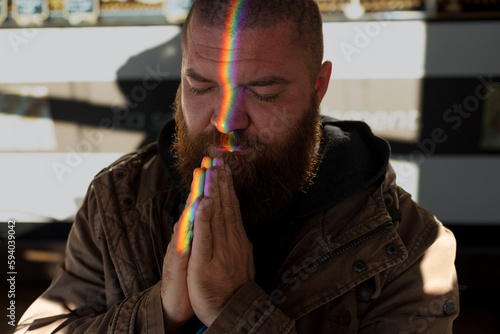 Portrait of bearded man praying, with a glare of light in the form of a rainbow on his face - a symbol of the LGBT people community