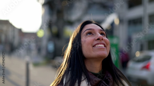 One hopeful young woman standing in street looking at sky with HOPE and FAITH. Happy female person in 20s stands in urban setting closeup face portrait © Marco