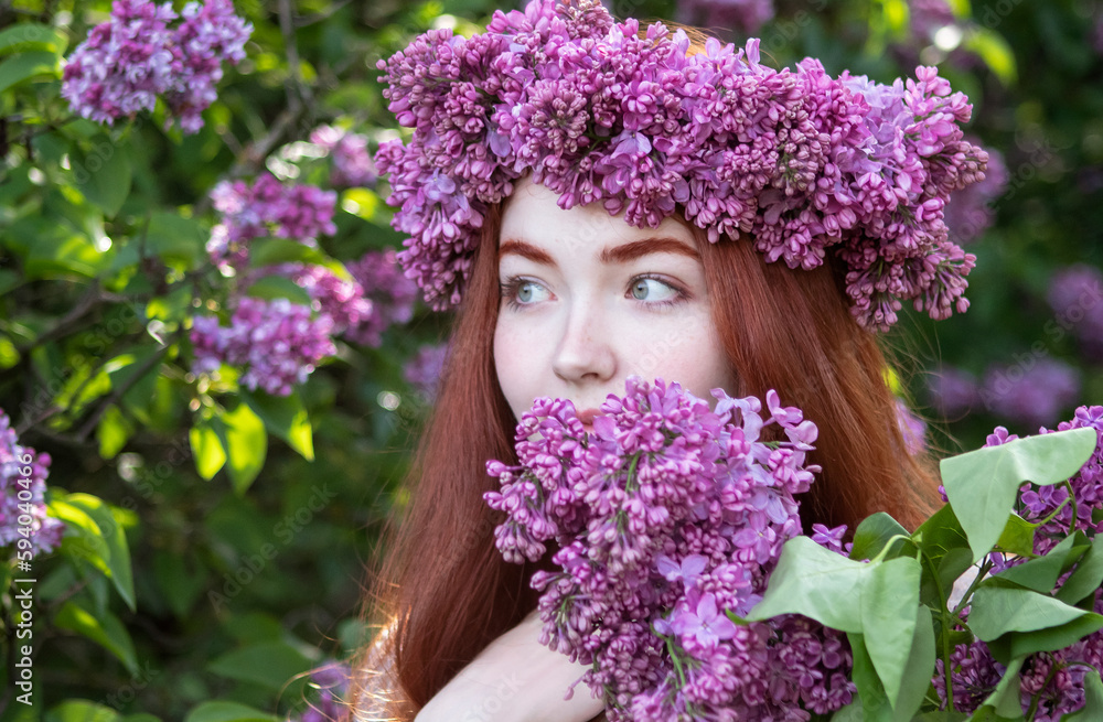 young girl with long red hair with a wreath of lilacs on her head in the garden in spring young girl with long red hair with a wreath of lilacs on her head in the garden in spring