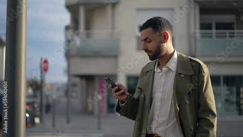 One Middle Eastern young man standing in city street checking phone. An Arab male person looking at online content outside