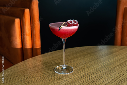 Summer cocktail garnished with raspberry berries. Pink cold beverage on bar terrace.