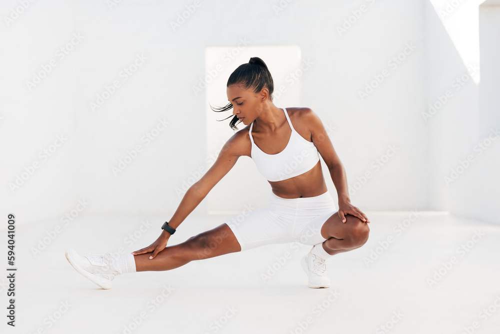 Fototapeta premium Woman in white fitness attire warming up her body and legs. Female doing stretching exercises in white outdoor studio.