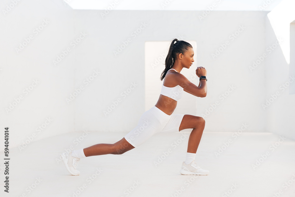 Fototapeta premium Side view of a slim woman in white sportswear stretching her legs. Young female in white outdoor studio warming up her body.
