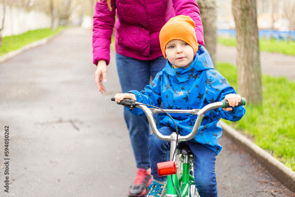 Young mom teaching son to ride bike first time in park Young mom teaching son to ride bike first time in park