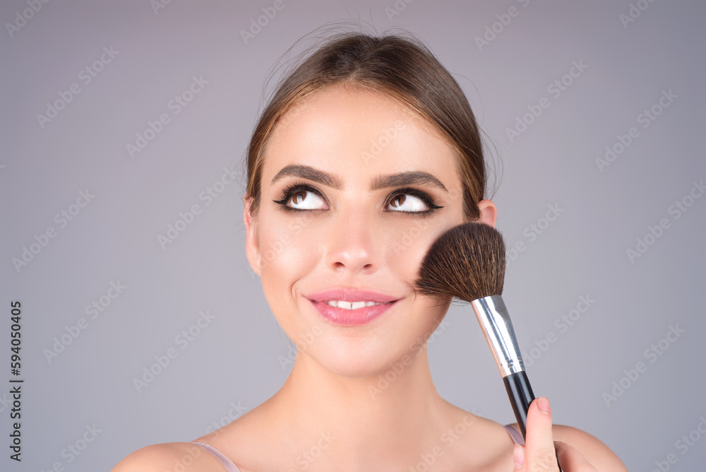 Girl hold blush blusher apply powder visage isolated over studio background. Young woman powdering cheeks. Makeup brush. Female model gets blush powder on the cheekbones. Girl hold blush blusher apply powder visage isolated over studio background. Young woman powdering cheeks. Makeup brush. Female model gets blush powder on the cheekbones.