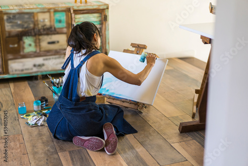 Woman artist painting on a canvas a blue abstract painting. Creative ywoman working on the floor in her art studio. photo