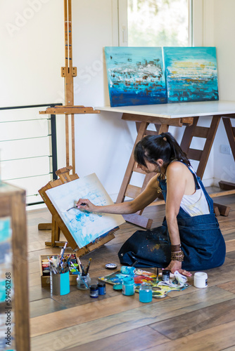 Woman artist painting on a canvas a blue abstract painting. Creative ywoman working on the floor in her art studio. photo