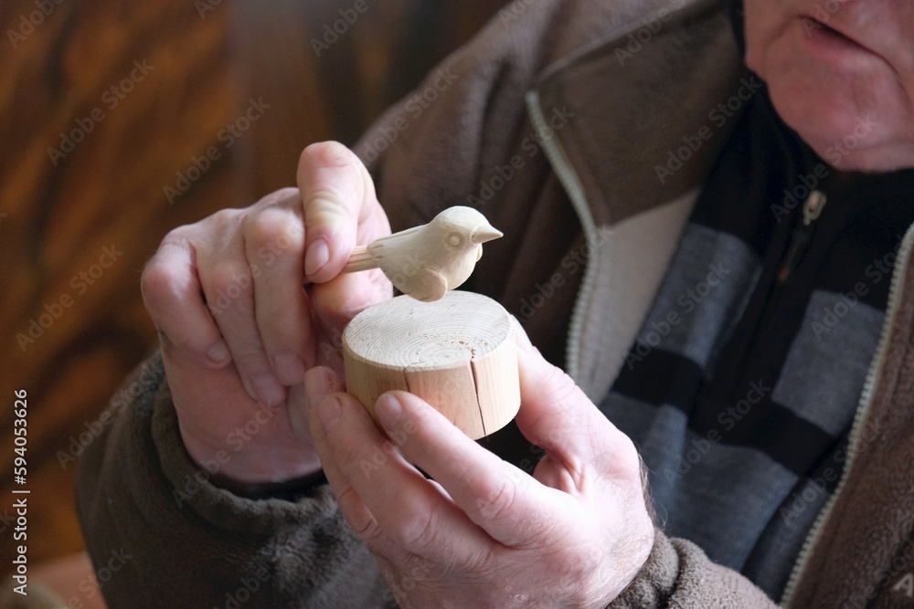 Old man is holding small bird carved in light wood.