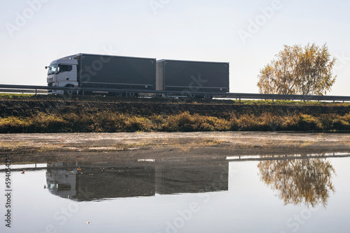 Truck goes on the road in autumn. car transport . Truck with semi-trailer in gray color. Transport truck drives in autumn by the lake.