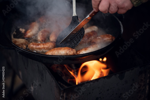 Cooking sausages on fire in a large frying pan outdoors.