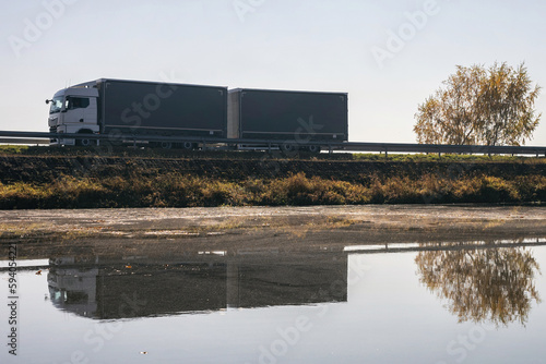 Truck goes on the road in autumn. car transport . Truck with semi-trailer in gray color. Transport truck drives in autumn by the lake.