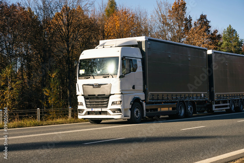 Truck is driving through the forest in autumn. Car transport . Truck with semi-trailer in gray color.