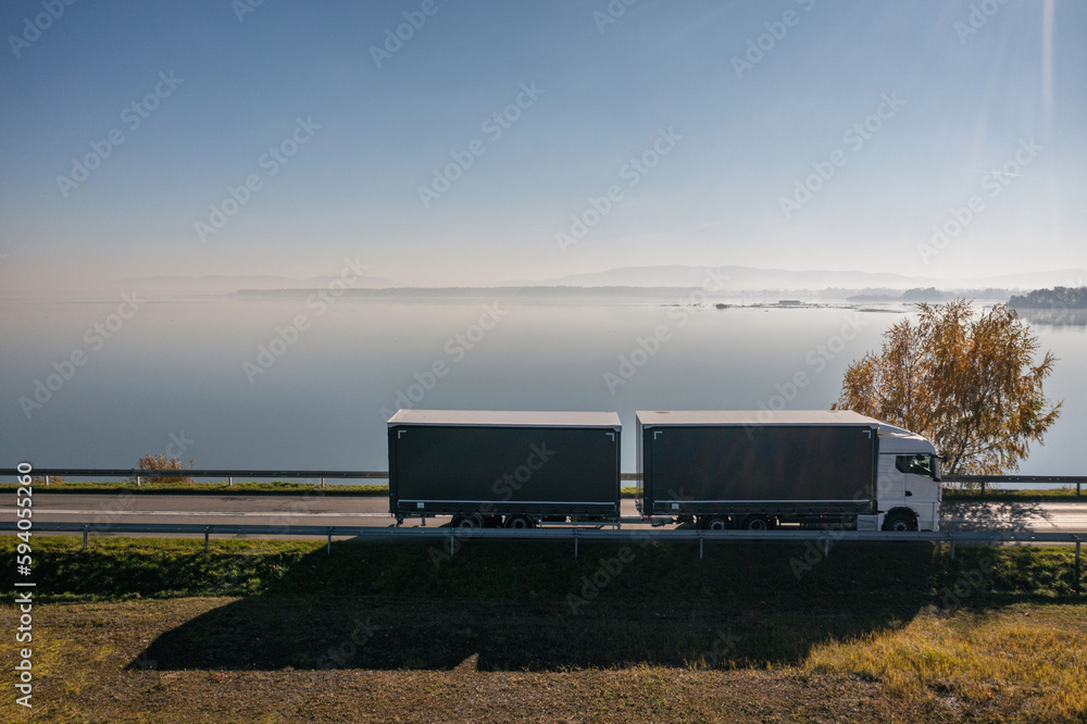 Truck goes on the road in autumn. car transport . Truck with semi-trailer in gray color. Transport truck drives in autumn by the lake. Truck goes on the road in autumn. car transport . Truck with semi-trailer in gray color. Transport truck drives in autumn by the lake.