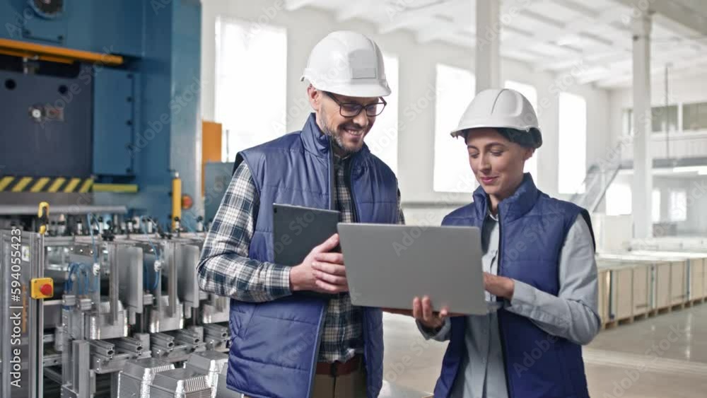 Good-looking Caucasian female in uniform blue vest white helmet showing information on her laptop to great middle-aged colleague wearing glasses. They talking speaking discussing. Good-looking Caucasian female in uniform blue vest white helmet showing information on her laptop to great middle-aged colleague wearing glasses. They talking speaking discussing.