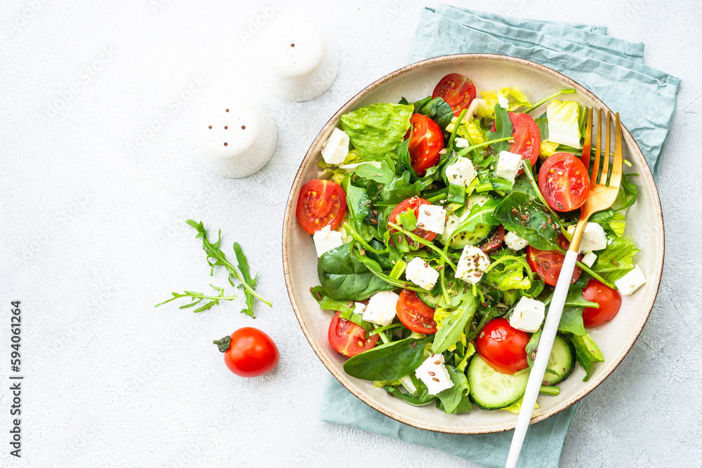 Green salad with spinach, arugula, tomatoes and feta with olive oil. Top view on white. Green salad with spinach, arugula, tomatoes and feta with olive oil. Top view on white.