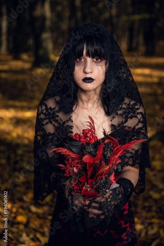 Vertical portrait of a scary corpse bride holding red flowers in the autumn forest