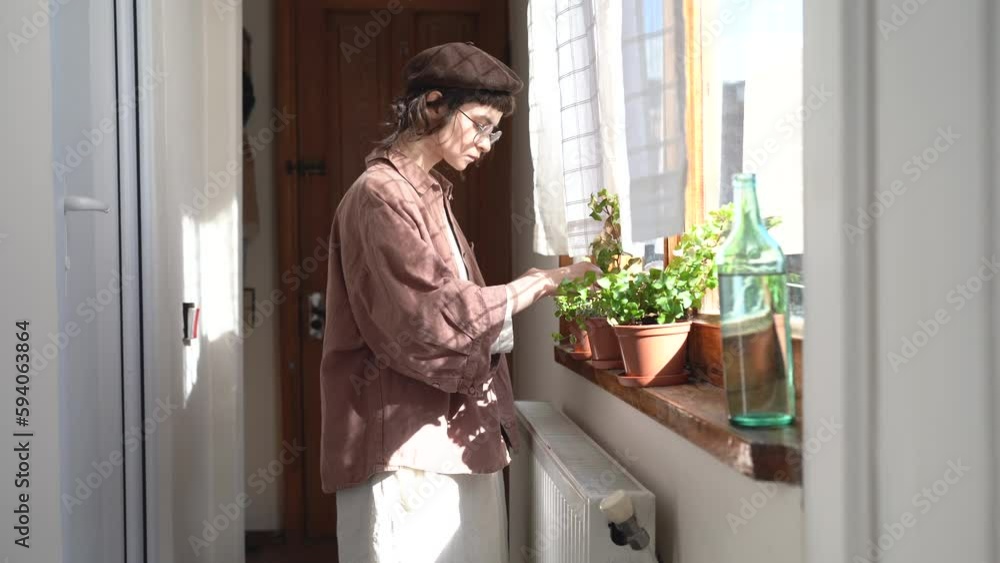 Young woman in retro style clothes housekeeping watering plants on windowsill at home. Caring girl pouring water potted flower, enjoying growing plants. Taking care for houseplants, hobby concept. Young woman in retro style clothes housekeeping watering plants on windowsill at home. Caring girl pouring water potted flower, enjoying growing plants. Taking care for houseplants, hobby concept.