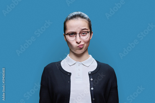 Surprised puzzled teenage girl looking at camera on blue background
