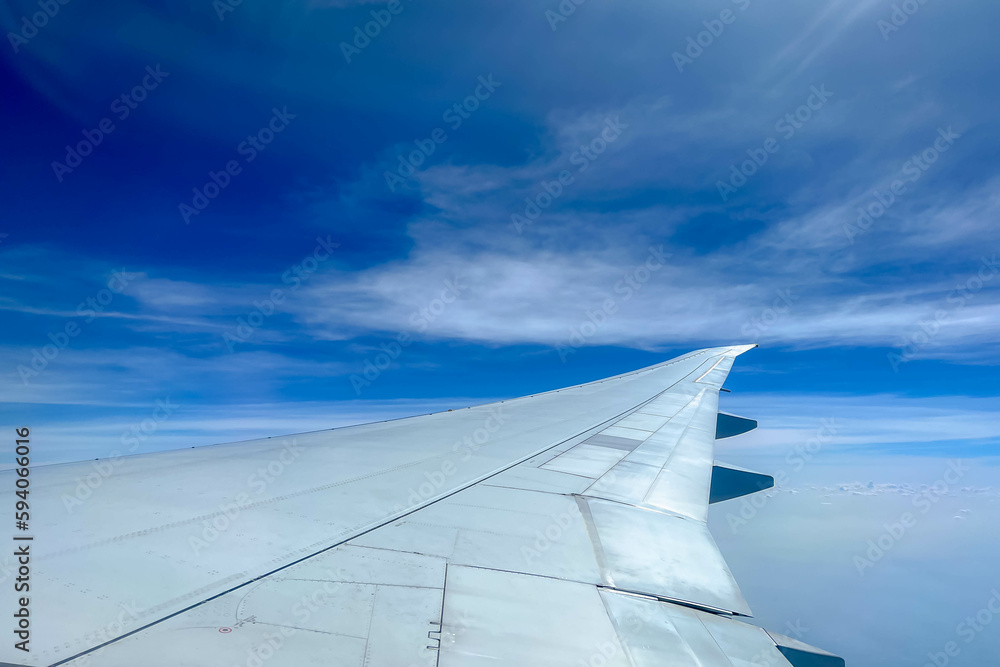 View from the airplane window flying above the sky with white puffy clouds, Wing of aircraft with blue sky as background.