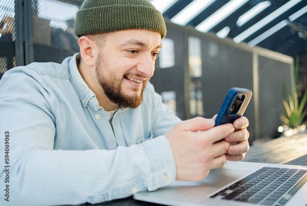Portrait of cheerful blogger with cellphone and laptop technology enjoying freelance lifestyle, happy hipster guy using mobile phone and netbook in cafe Portrait of cheerful blogger with cellphone and laptop technology enjoying freelance lifestyle, happy hipster guy using mobile phone and netbook in cafe