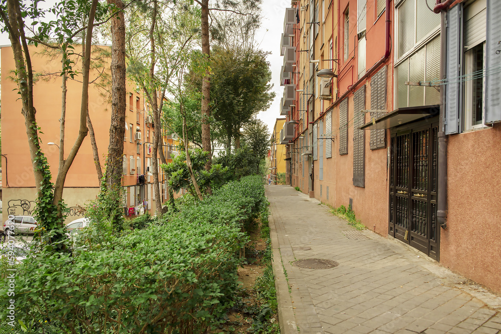 Urban sidewalk that passes in front of the access portals to residential buildings with hedges and trees in front