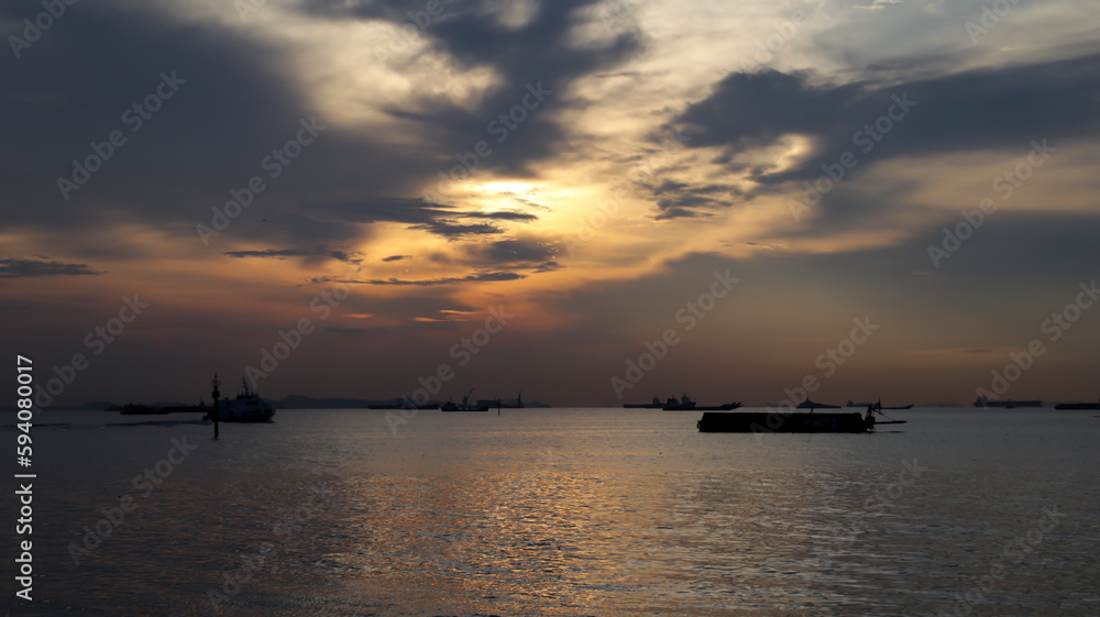 Sunset at the harbor of industrial area, silhouette of barge, fast ferry, large logistic ship.