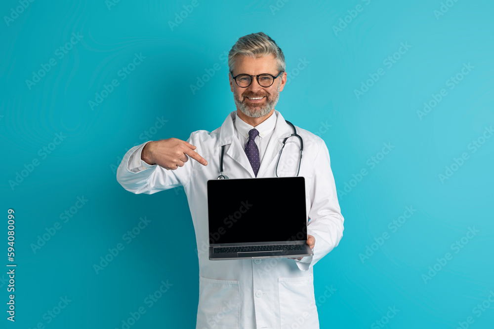Smiling grey-haired caucasian doctor showing laptop with blank screen Smiling grey-haired caucasian doctor showing laptop with blank screen