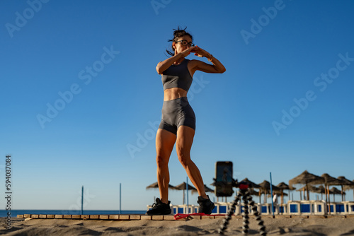 a beautiful girl goes in for sports does functional training exercises on the seashore at dawn and takes pictures of herself on the phone. stream. online training