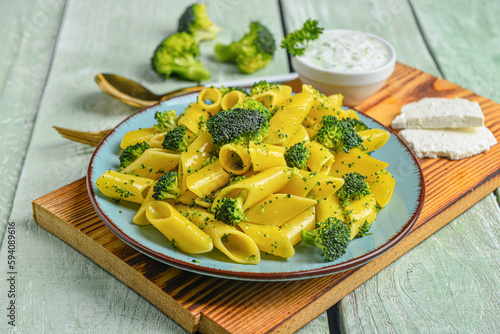 Plate with tasty pasta and broccoli on green wooden background