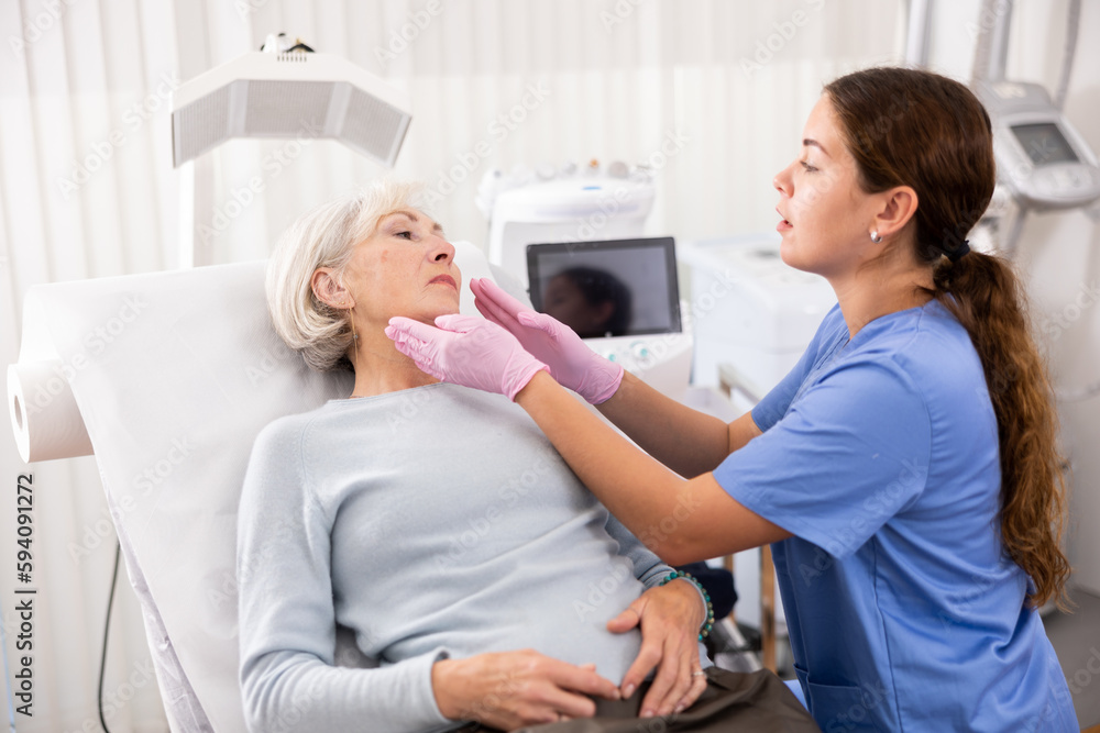 Fototapeta premium Mature woman lying on couch during consultation with female beautician, checking her skin before medical intervention in esthetic clinic