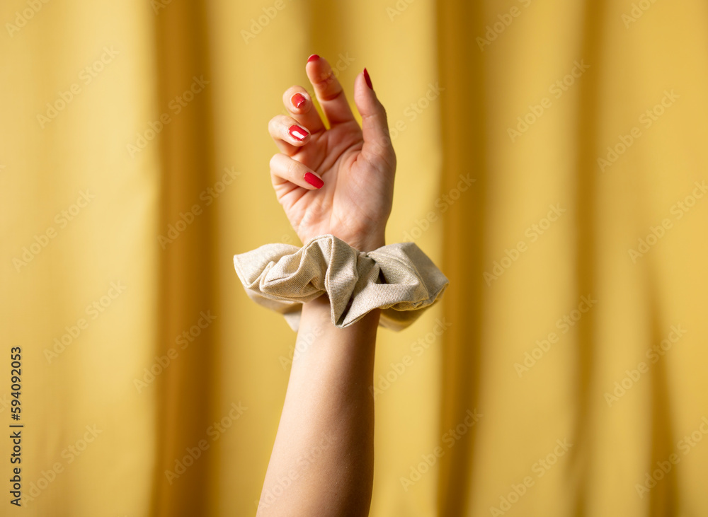 Woman is wearing scrunchies around their wrists in yellow background.