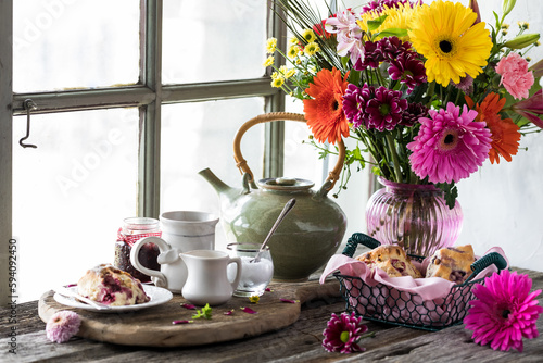 Tea and scones on a rustic wooden table with a bouquet of beautiful flowers.