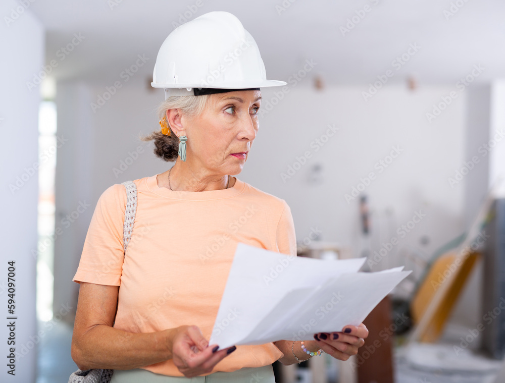 Focused mature woman owner of house being renovated reading plans, examining space and developing space planning concept