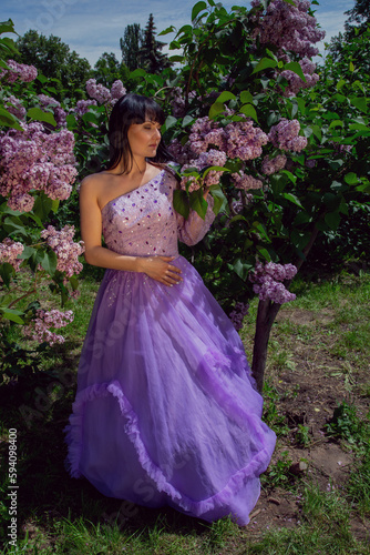 Young brunette woman in a beautiful dress in a garden with blooming purple bushes.