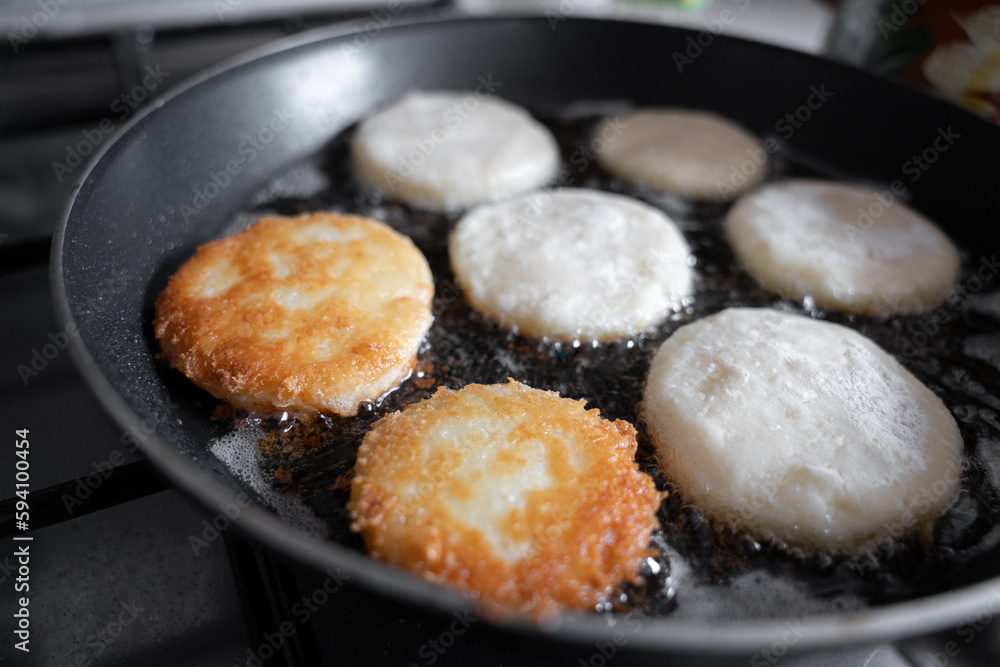 Some potato cakes are being fried in a sauce pan with vegetable oil