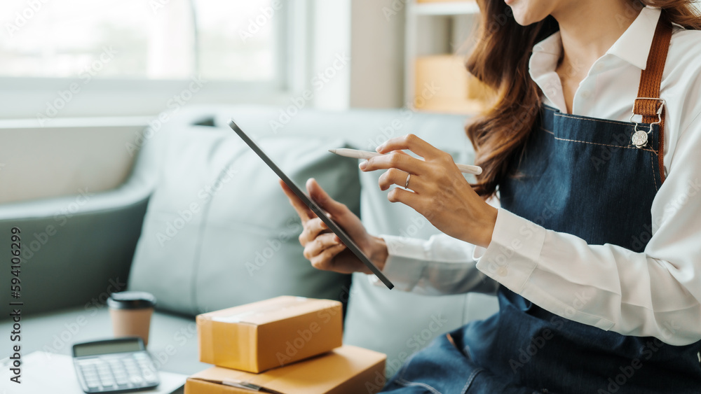 Using tablet computer, Young pretty Asian female influencer small businesses SME owners female entrepreneurs working on receipt box and check online orders, sitting on sofa of home online business. Using tablet computer, Young pretty Asian female influencer small businesses SME owners female entrepreneurs working on receipt box and check online orders, sitting on sofa of home online business.